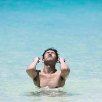透明な海に胸まで浸かって両腕を伸ばし顔を上げる男性の写真