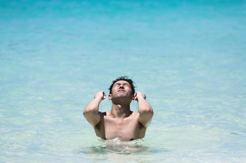 透明な海に胸まで浸かって両腕を伸ばし顔を上げる男性