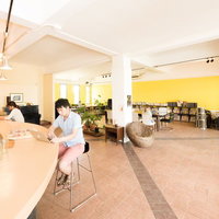 木製カウンターのコワーキングカフェで作業する男性と奥の女性の写真