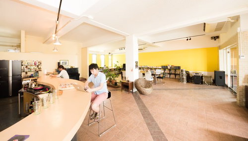 木製カウンターのコワーキングカフェで作業する男性と奥の女性