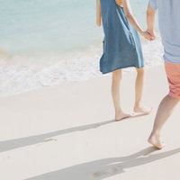 透明な海の浅瀬を手をつないで歩く恋人と砂浜の足あとの写真