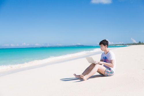 海で楽しそうに泳ぐ同僚を見ながら、ひざの上にMacBook Airを乗せて改修案件をするエンジニア