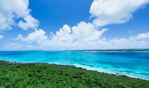高い位置から見下ろす宮古島の緑の海岸線と青い海と雲