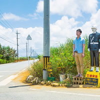 交通安全の看板の前で警察マネキンと並ぶ青シャツの男性の写真