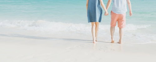 青い海の波打ち際で手をつなぐデニムワンピースのカップル