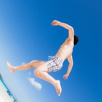 青空の下で飛び込み台からジャンプする海水パンツの男性の写真