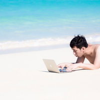 前浜ビーチの白い砂浜でうつ伏せにノートPCを操作する男性の写真