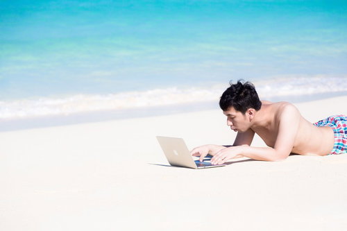 前浜ビーチの白い砂浜でうつ伏せにノートPCを操作する男性