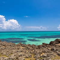 でこぼこした岩場の先に広がる池間島のエメラルドグリーンの海の写真