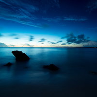 穏やかな海と日没、水平線に沈む夕日、岩場の風景の写真