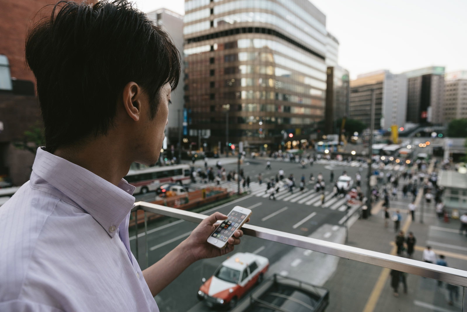 駅前でスマートフォンを操作する白いシャツの男性［モデル：Tsuyoshi.］