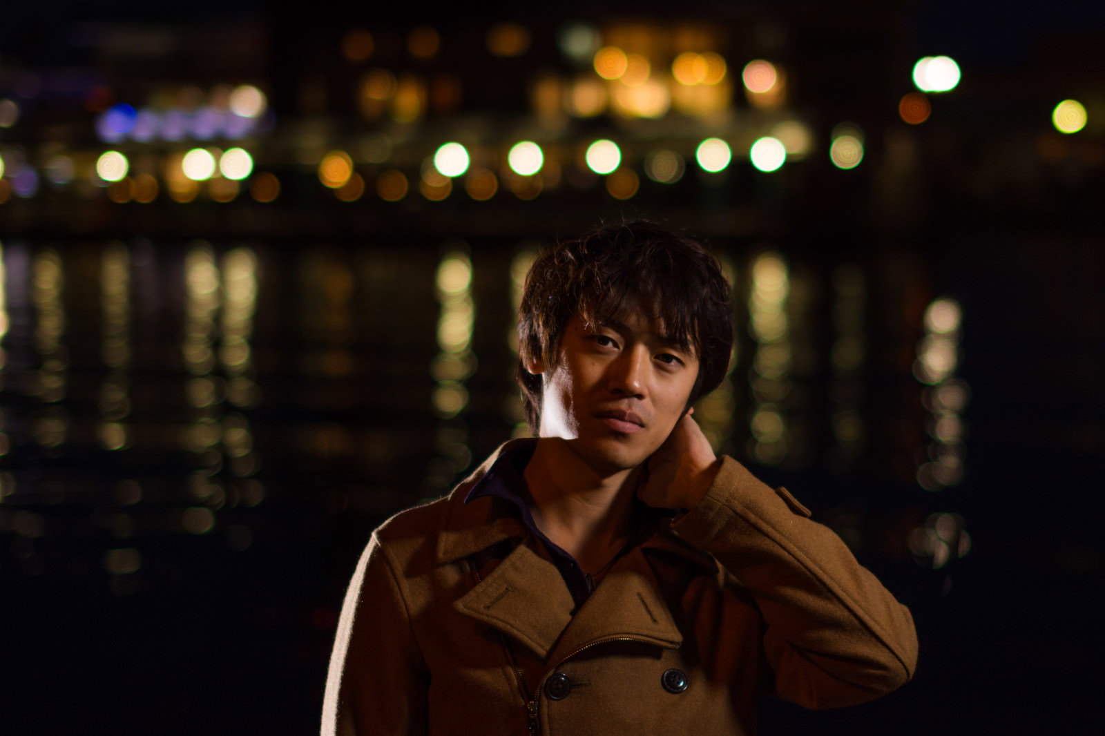 夜景を背景に首に手を当てる男性［モデル：Tsuyoshi.］