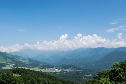 霞ゆく山々と街並みが見える青空と入道雲の風景
