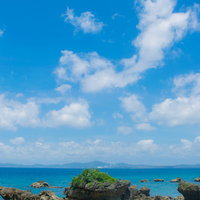 夏の海岸に点在する岩礁と青空、白い雲が浮かぶ風景の写真
