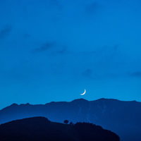 夜空に浮かぶ三日月と山のシルエット、星空が輝く夜間風景の写真