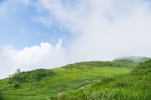 高原に立ち込める白い雲と緑の草原、背景に連なる山々