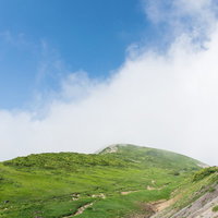 青空と雲が広がる稜線を歩く登山者たちの姿の写真