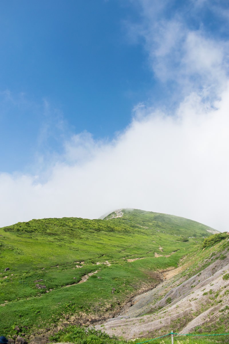 青空の下、緑の稜線を歩く登山者のシルエット