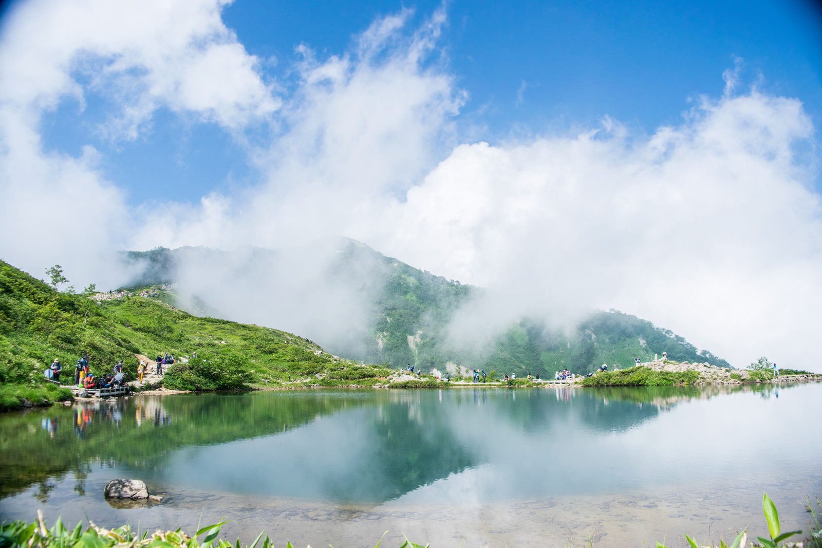 湖面に映る山と霧、休憩する登山者たちの風景