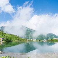 湖面に映り込む雲と山頂付近の登山者が休憩する風景の写真