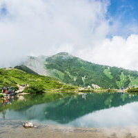 緑の山々に囲まれた湖の周りでカメラを構える登山者達の写真