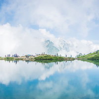 沸き立つ雲のリフレクションと湖畔の登山者の列の写真