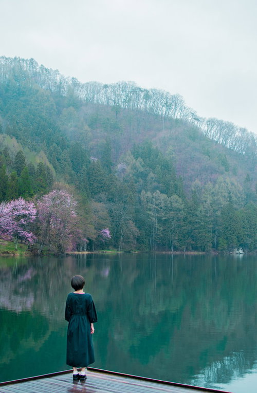 水鏡に映る山々と湖畔に佇む後ろ姿の女性のシルエット