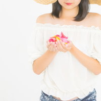 麦わら帽子を被って花びらに想いを込める女性の写真