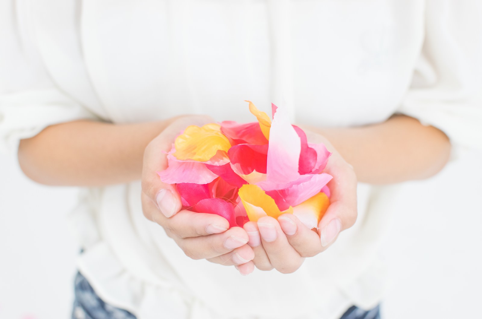 白い服を着た女性が両手のひらにピンクと黄色の花びらを集めている