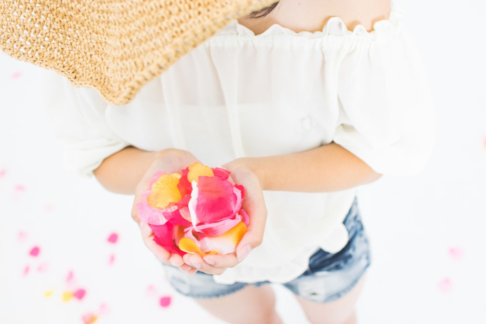 白いトップスを着た女性が両手にピンクの花びらを持っている写真