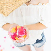 両手いっぱいに広げたピンクの花びら、白いトップスを着た女性の写真