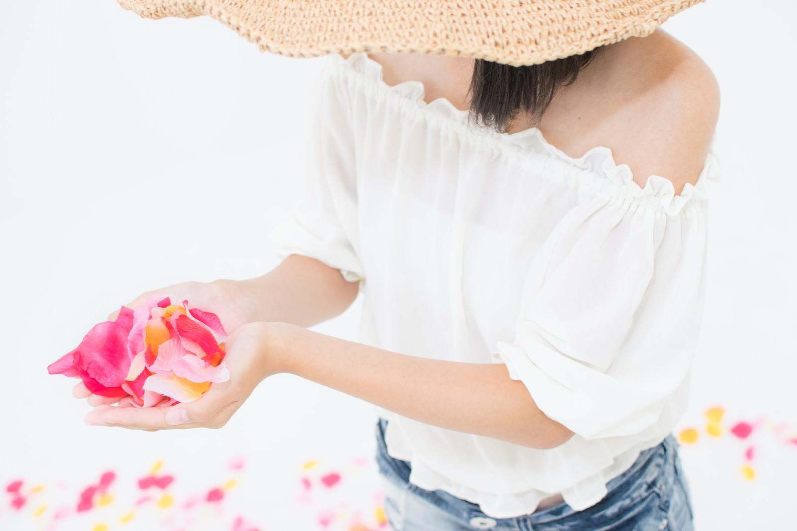 白い服を着た女性が両手でピンクの花びらを持ち、花びらがこぼれ落ちている様子
