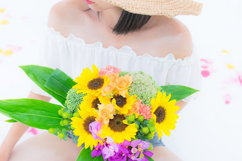 ヒマワリのブーケを持ちオフショルダートップスを着た女性