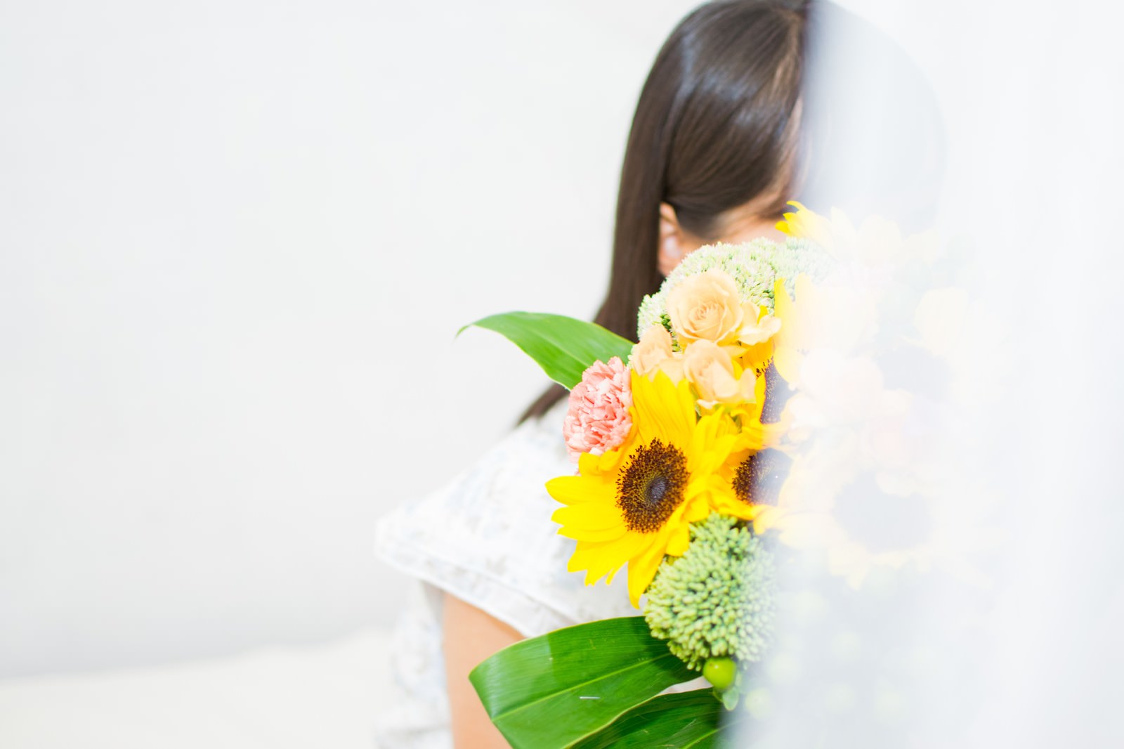 黄色いひまわりの花束を持って立つ白い服の女性