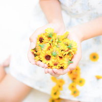 小さな黄色い向日葵の造花を両手で包み込む女性の写真