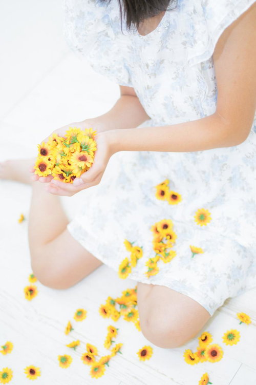 小さな黄色いひまわりを両手いっぱいに持つ女性