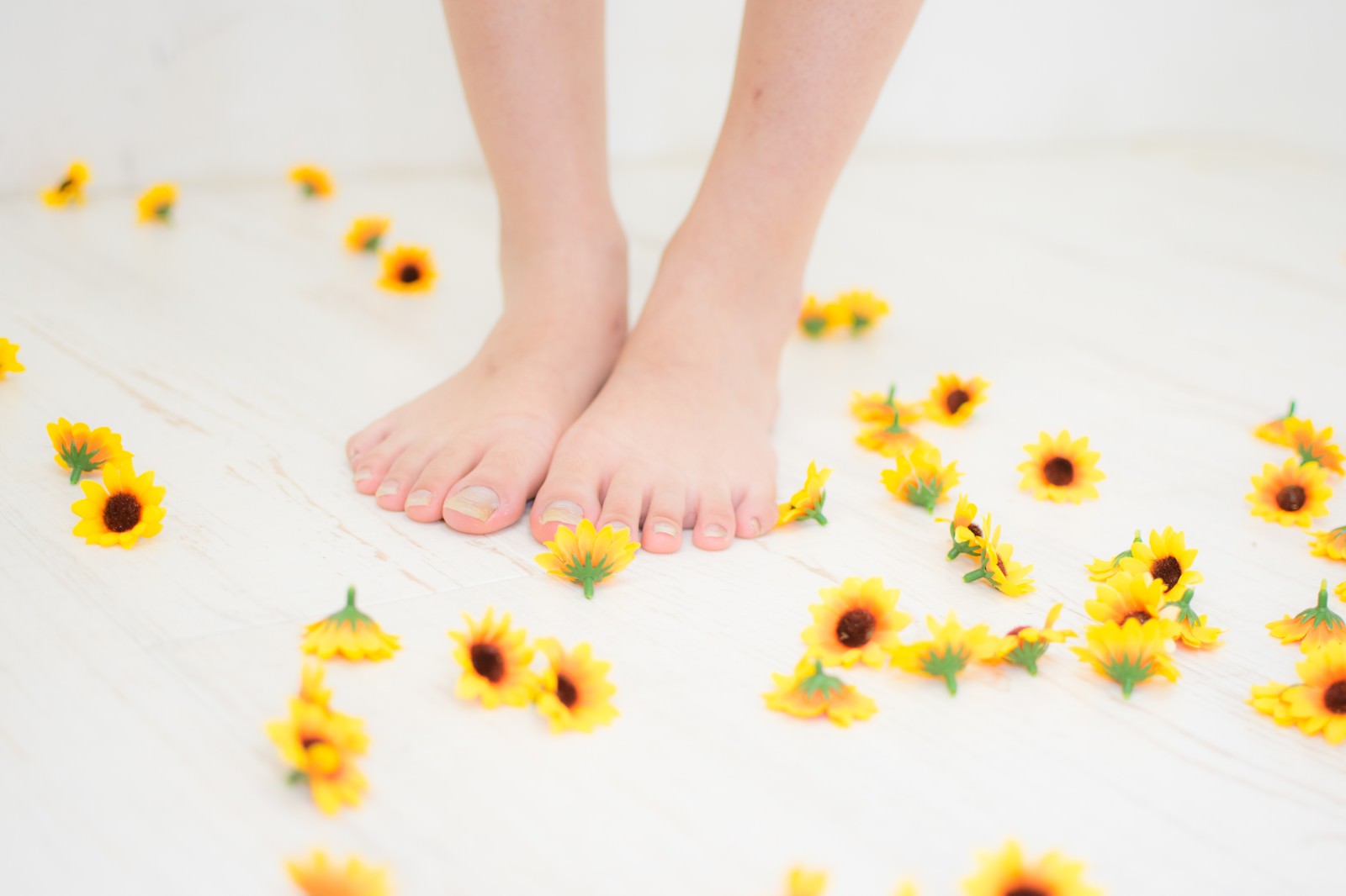白い床に散らばる黄色いひまわりのブローチと素足の足元