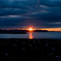 厚い雲間から現れる朝日と海面に映る光の夜明け風景の写真