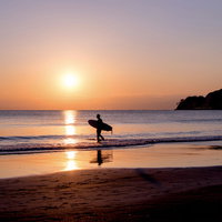夕暮れの海に向かうサーファーのシルエットの写真