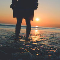 夕焼け空を見つめる女性と崩れて泡立つ波の浜辺風景の写真