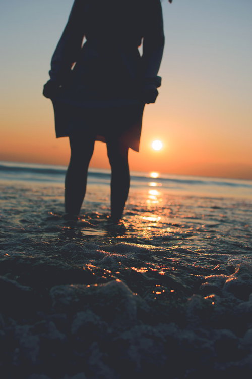 夕焼け空を見つめる女性と崩れて泡立つ波の浜辺風景