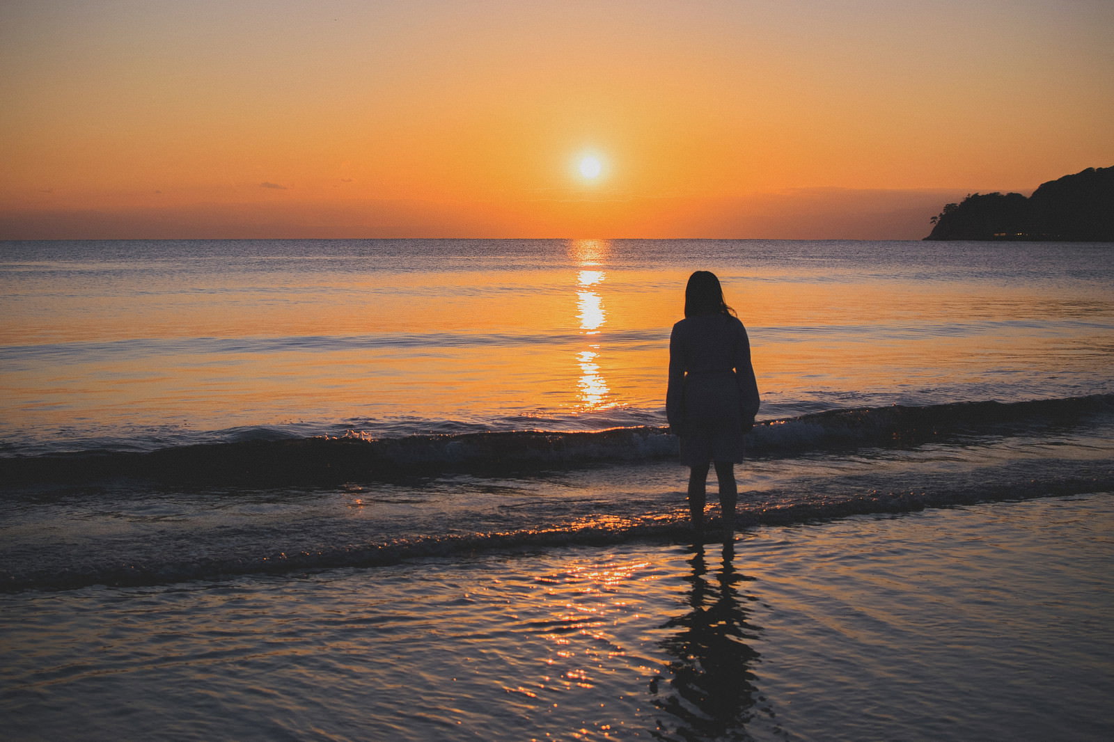 夕焼けの浜辺で海に向かって立つ女性のシルエット