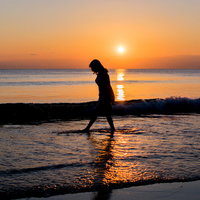 夕暮れの浜辺に立つ女性のシルエットの写真