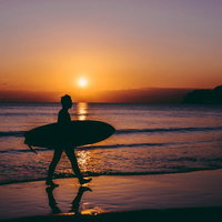 夕焼けに染まる海から上がるサーファー男性のシルエットの写真