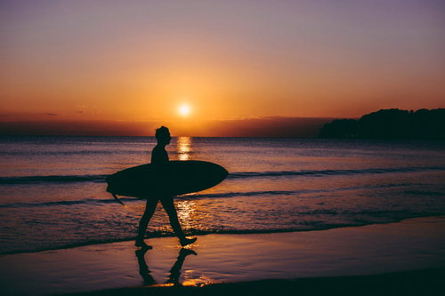 夕焼けに染まる海から上がるサーファー男性のシルエット