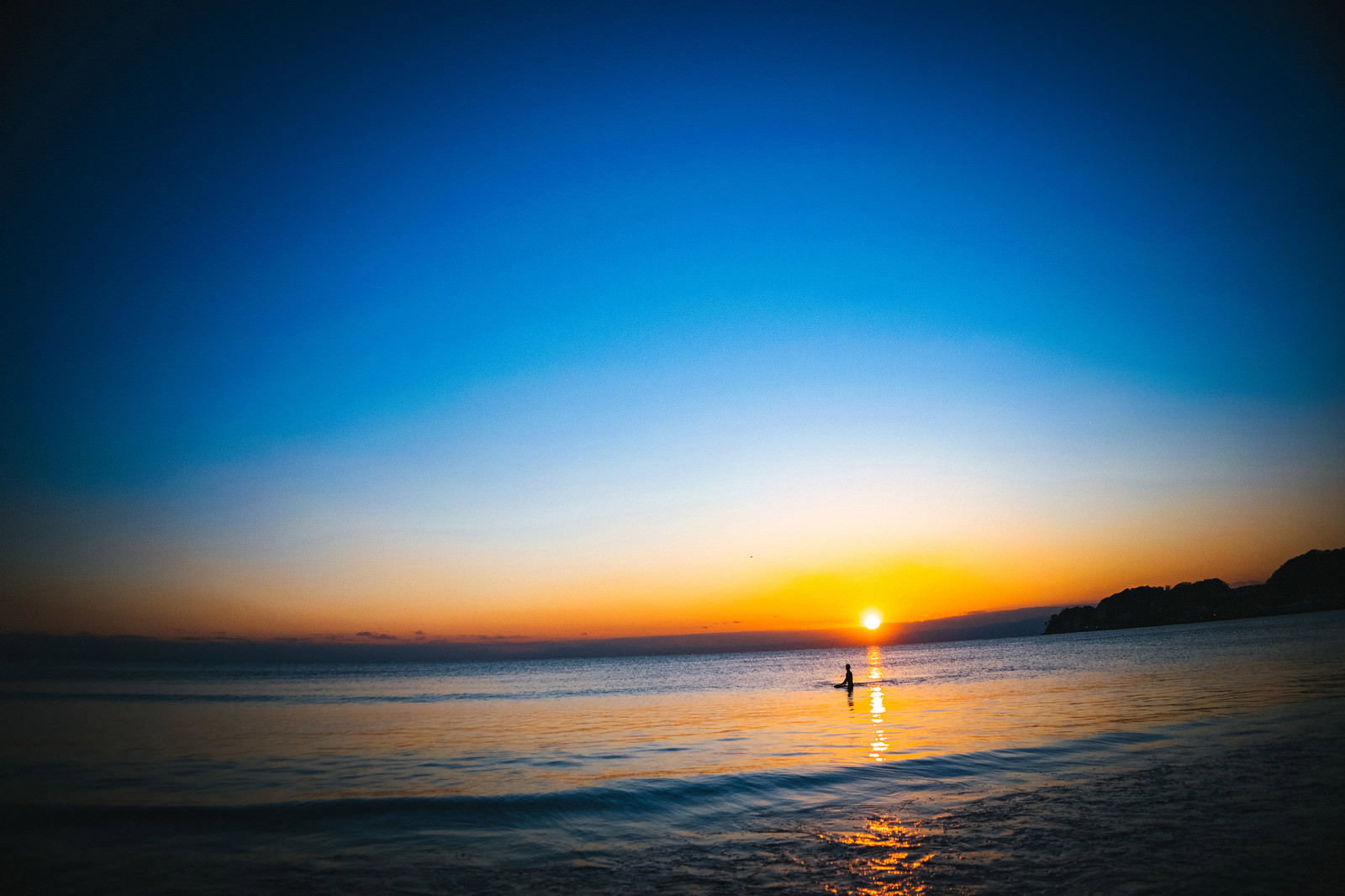 夕日の焼けた海でサーフボードの上に立つサーファーのシルエット