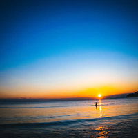 夕日の焼けた海に浮かぶサーファーのシルエットの写真