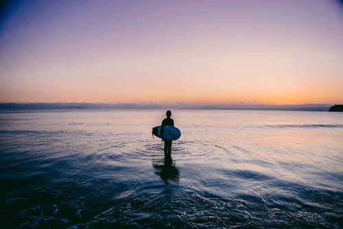 夕暮れの海でサーフボードを持つサーファーのシルエット