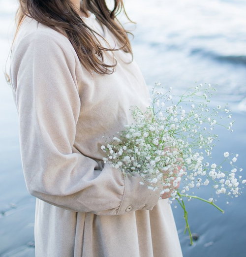 海辺で白いカスミソウを抱える女性、波打ち際に立つ