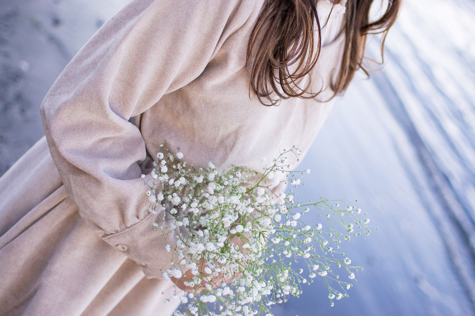 白いカスミソウの花束を両手で抱える薄いピンクの服を着た女性